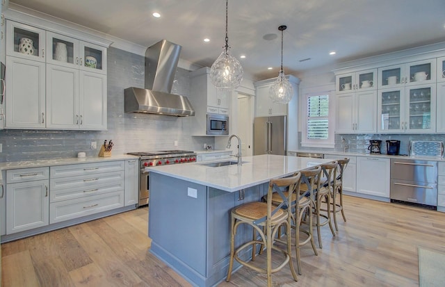 kitchen featuring premium appliances, sink, wall chimney range hood, decorative light fixtures, and white cabinets