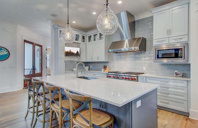 kitchen featuring french doors, an island with sink, sink, and wall chimney range hood