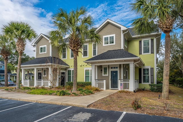 townhome / multi-family property with covered porch, a shingled roof, and uncovered parking