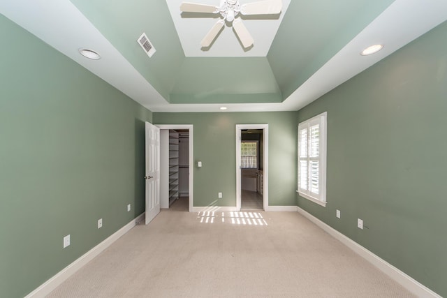 unfurnished bedroom featuring vaulted ceiling, a spacious closet, a raised ceiling, light carpet, and a closet