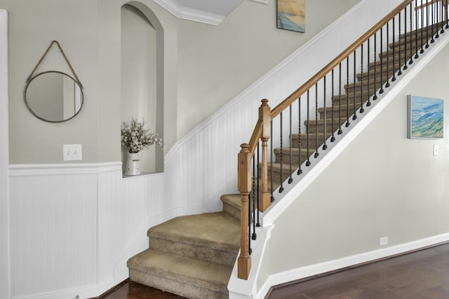 stairs with ornamental molding, wainscoting, wood finished floors, and a towering ceiling