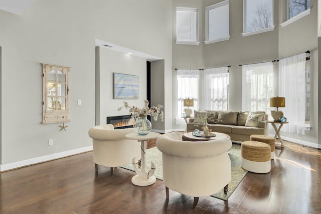 living area featuring wood finished floors, a glass covered fireplace, a high ceiling, and baseboards