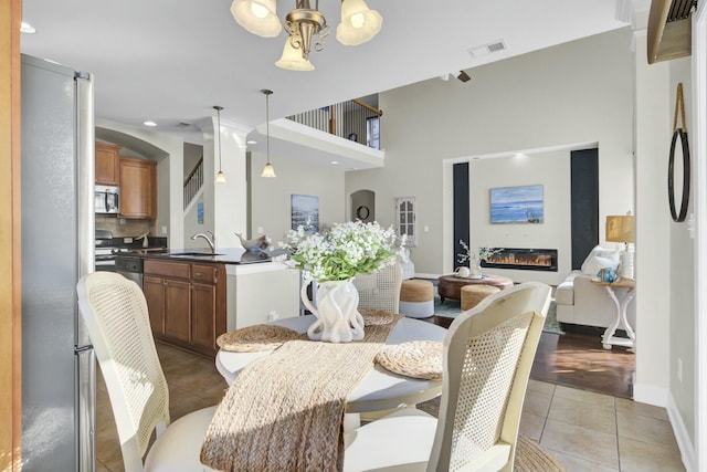 dining space featuring light tile patterned floors, baseboards, visible vents, a glass covered fireplace, and a towering ceiling