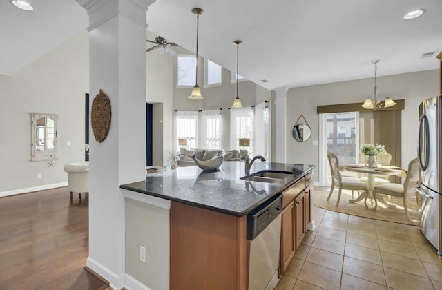 kitchen with brown cabinets, appliances with stainless steel finishes, a sink, dark stone countertops, and ornate columns