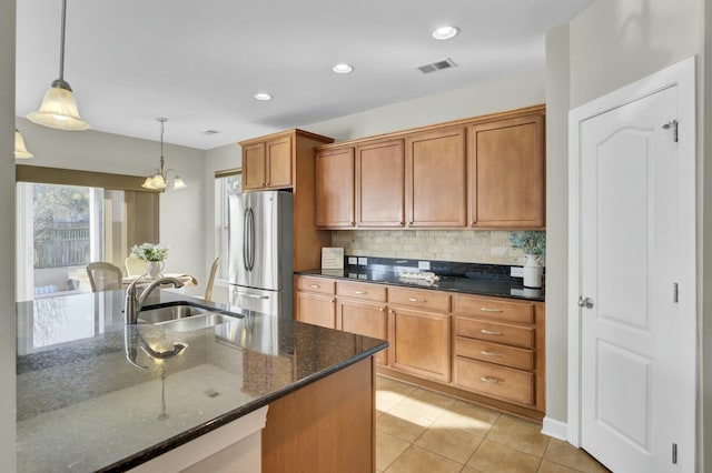 kitchen with visible vents, backsplash, brown cabinetry, freestanding refrigerator, and a sink