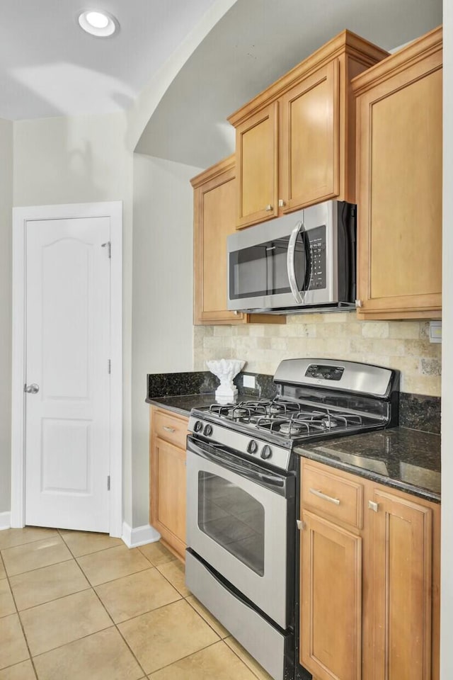 kitchen featuring light tile patterned floors, appliances with stainless steel finishes, dark stone countertops, and decorative backsplash