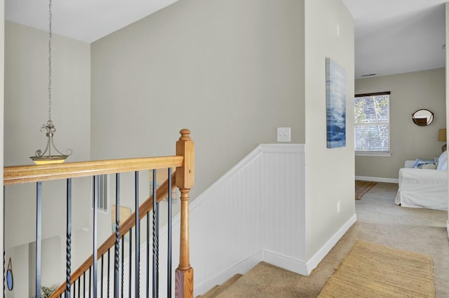 corridor featuring a wainscoted wall, carpet flooring, and an upstairs landing