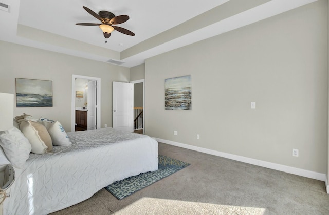 carpeted bedroom featuring a tray ceiling, visible vents, a ceiling fan, ensuite bath, and baseboards