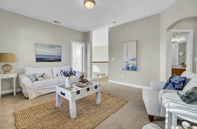 carpeted living area featuring arched walkways, visible vents, and baseboards