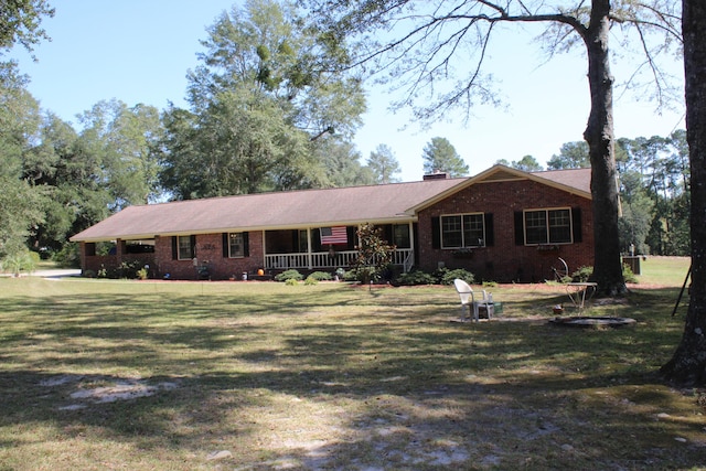 ranch-style house featuring covered porch, brick siding, a chimney, and a front lawn