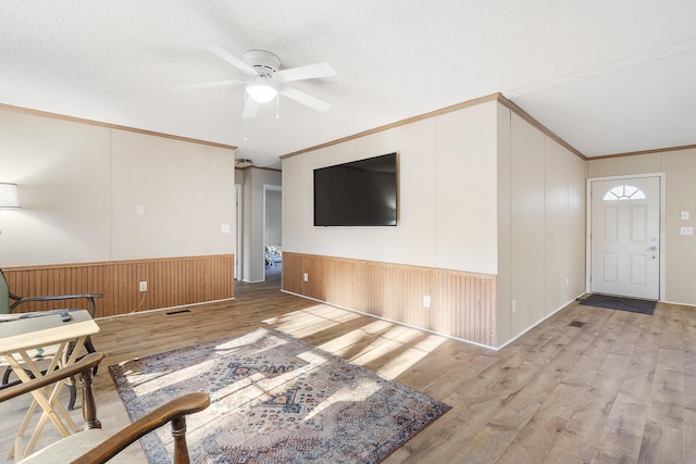 foyer entrance with a textured ceiling, crown molding, wainscoting, ceiling fan, and wood finished floors