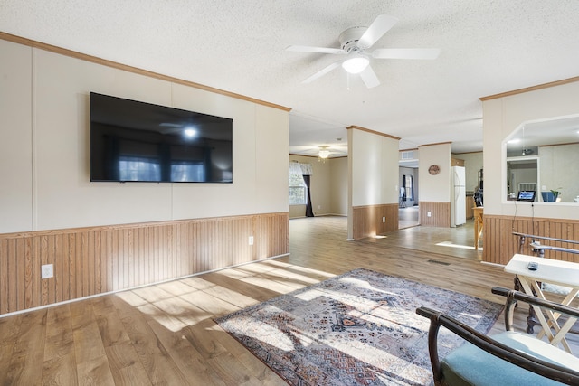 unfurnished living room with crown molding, ceiling fan, wainscoting, and a textured ceiling