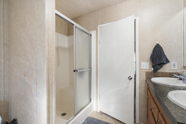 bathroom with a stall shower, double vanity, a sink, and tile patterned floors