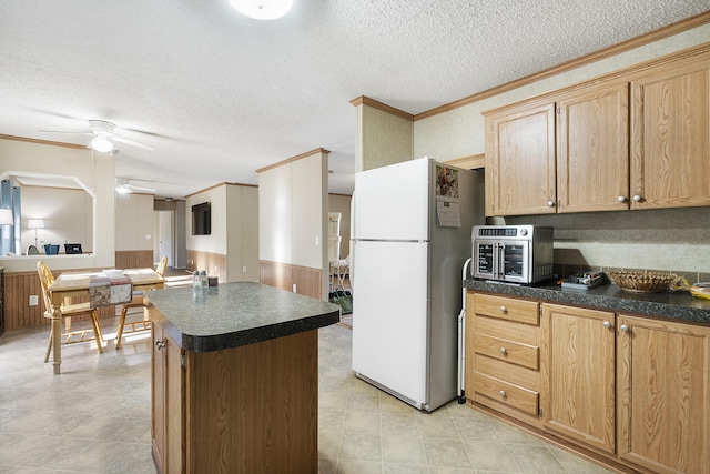 kitchen featuring freestanding refrigerator, crown molding, dark countertops, wainscoting, and ceiling fan