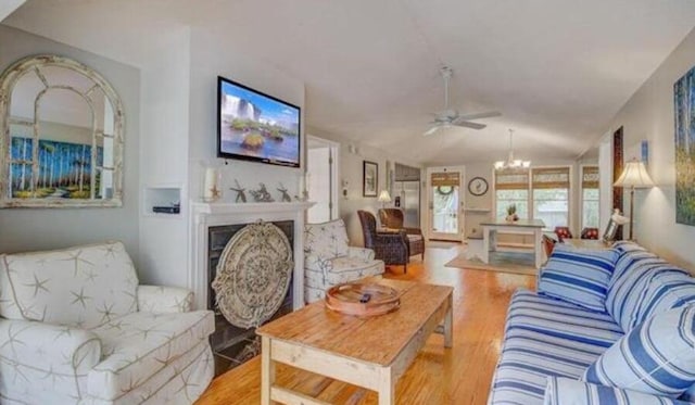 living room with ceiling fan with notable chandelier, light hardwood / wood-style floors, and vaulted ceiling