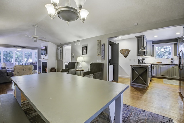 kitchen featuring gray cabinetry, stainless steel electric stove, ceiling fan with notable chandelier, vaulted ceiling, and tasteful backsplash