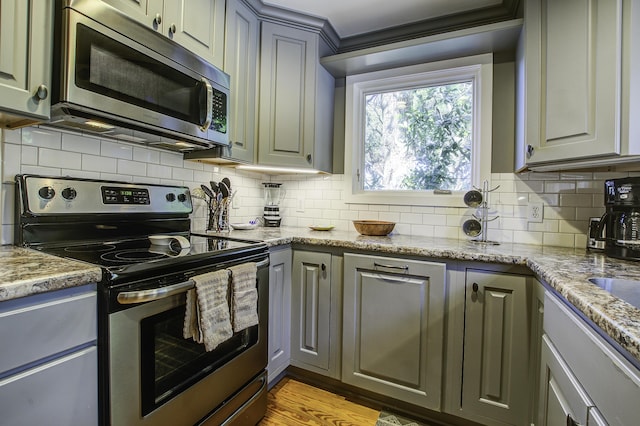 kitchen featuring gray cabinetry, decorative backsplash, light stone counters, and stainless steel appliances