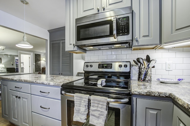 kitchen featuring appliances with stainless steel finishes, backsplash, light stone counters, pendant lighting, and gray cabinets