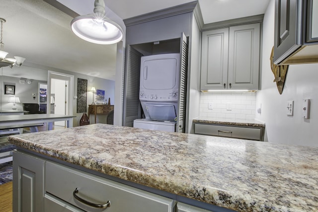 kitchen with tasteful backsplash, gray cabinetry, stacked washing maching and dryer, and decorative light fixtures