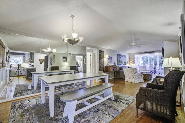 dining space with ceiling fan with notable chandelier, hardwood / wood-style flooring, and lofted ceiling