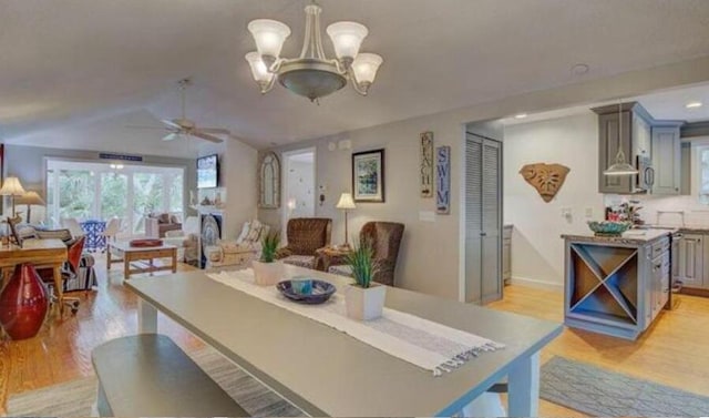 dining area featuring ceiling fan with notable chandelier, light hardwood / wood-style floors, and vaulted ceiling