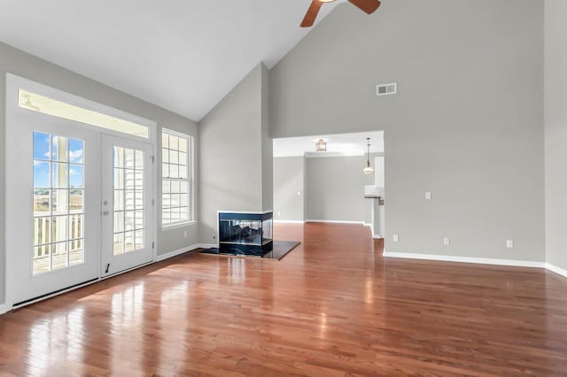 unfurnished living room featuring french doors, high vaulted ceiling, a multi sided fireplace, hardwood / wood-style flooring, and ceiling fan