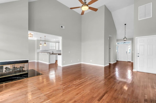 unfurnished living room featuring ceiling fan, a multi sided fireplace, high vaulted ceiling, and hardwood / wood-style floors