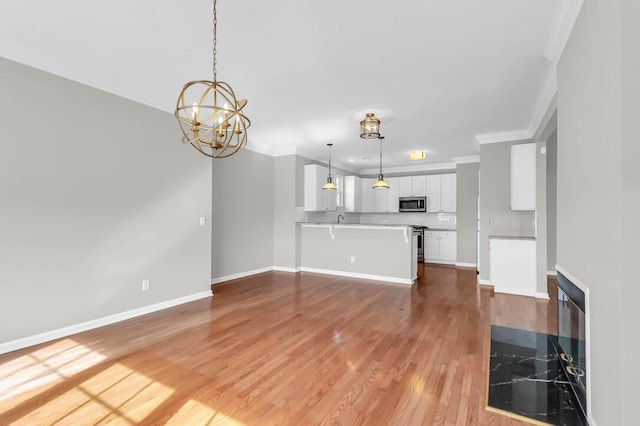 unfurnished living room featuring an inviting chandelier, ornamental molding, and wood-type flooring