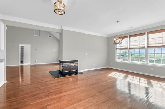 unfurnished living room with a multi sided fireplace, ornamental molding, wood-type flooring, and a notable chandelier