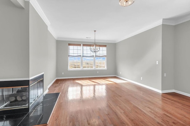 unfurnished living room with a tiled fireplace, crown molding, wood-type flooring, and a notable chandelier