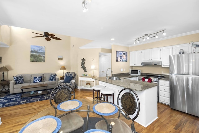 kitchen featuring ceiling fan, a kitchen bar, appliances with stainless steel finishes, white cabinets, and a sink