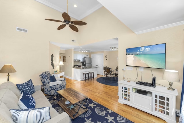 living room with visible vents, crown molding, light wood-type flooring, a towering ceiling, and a ceiling fan