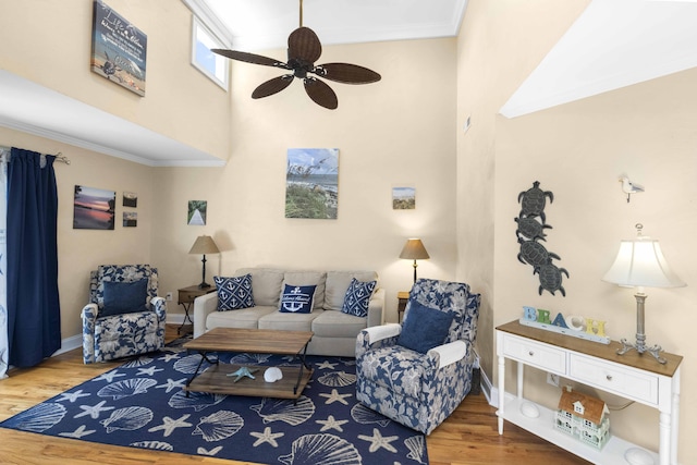 living room with wood finished floors, baseboards, ornamental molding, ceiling fan, and a towering ceiling