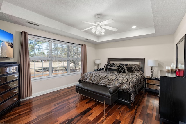 bedroom with ceiling fan, a tray ceiling, and dark hardwood / wood-style floors