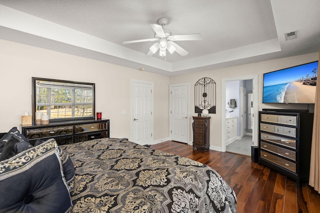 bedroom featuring connected bathroom, a raised ceiling, ceiling fan, dark hardwood / wood-style flooring, and a textured ceiling