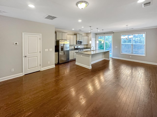 kitchen featuring light stone countertops, pendant lighting, stainless steel appliances, an inviting chandelier, and a kitchen island with sink