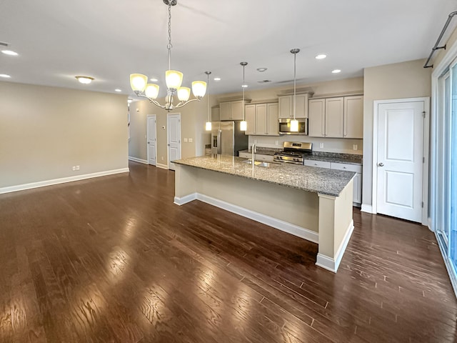 kitchen featuring stainless steel appliances, a kitchen island with sink, decorative light fixtures, light stone countertops, and sink