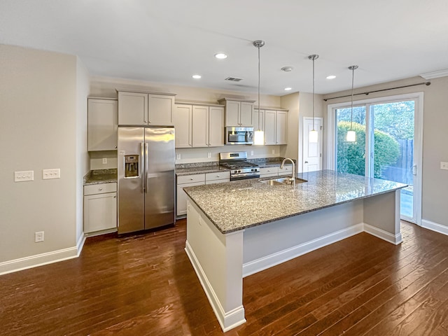 kitchen featuring stainless steel appliances, a kitchen island with sink, decorative light fixtures, light stone countertops, and sink