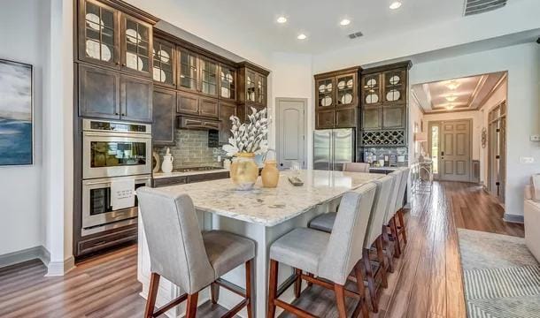 kitchen featuring hardwood / wood-style floors, a center island, appliances with stainless steel finishes, tasteful backsplash, and dark brown cabinets