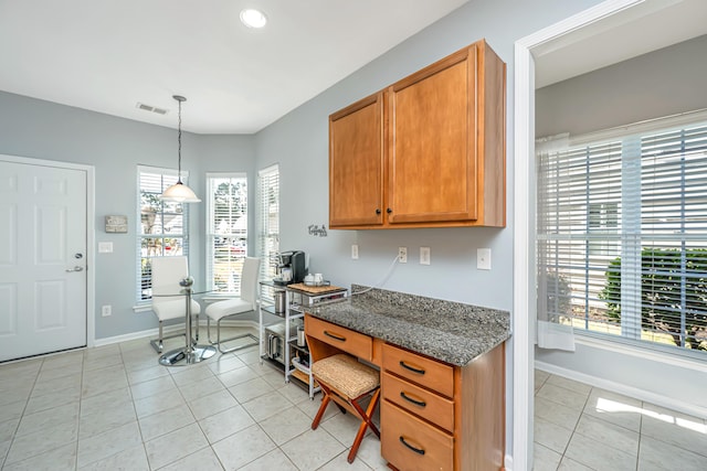 kitchen with visible vents, baseboards, light tile patterned floors, brown cabinetry, and built in study area