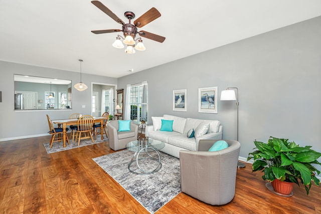 living room with a ceiling fan, baseboards, and wood finished floors