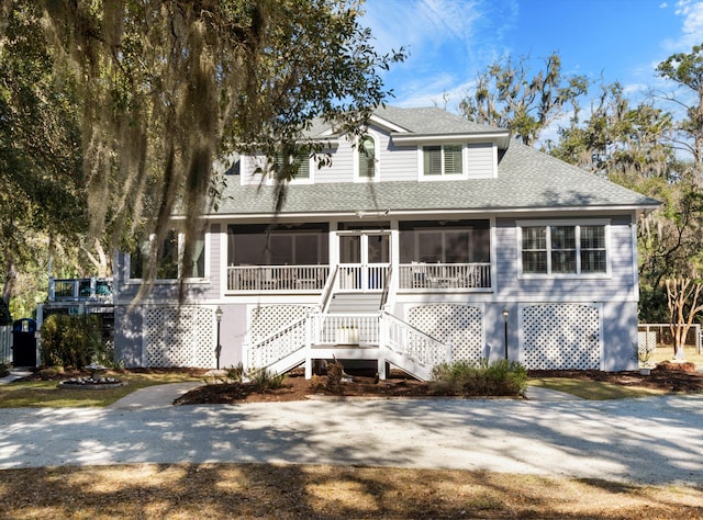 view of front of property with stairs, driveway, roof with shingles, and a sunroom