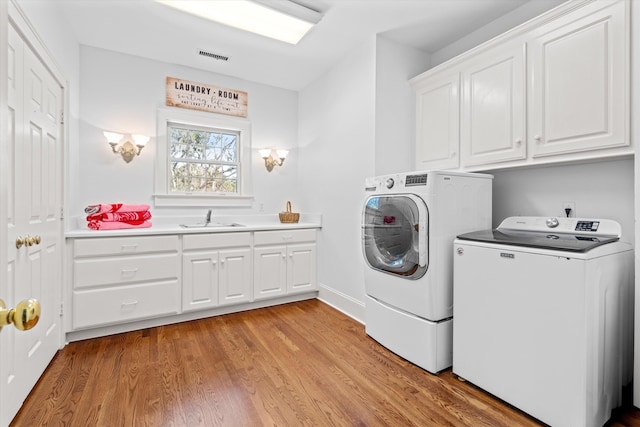 clothes washing area featuring cabinet space, visible vents, washer and dryer, light wood-style floors, and a sink