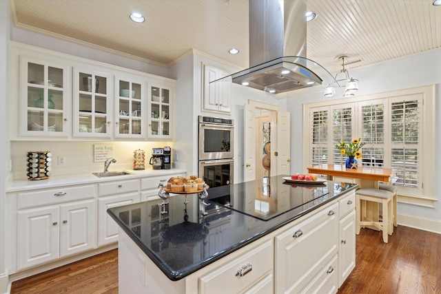 kitchen featuring island range hood, wood finished floors, black electric cooktop, stainless steel double oven, and a sink