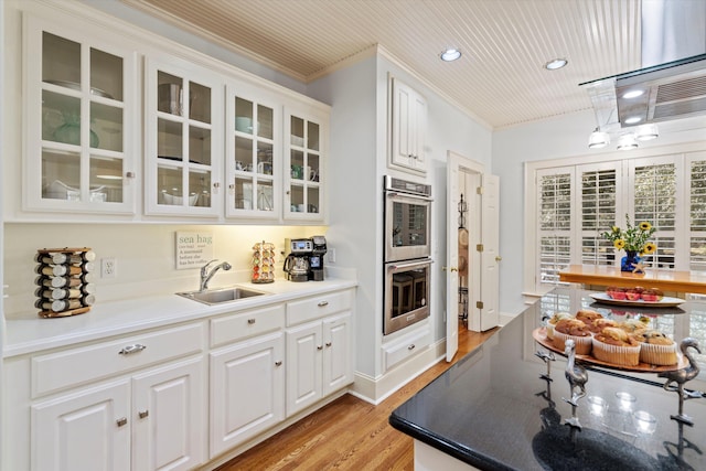 kitchen featuring glass insert cabinets, light wood-type flooring, double oven, white cabinetry, and a sink