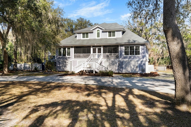 view of front facade featuring a sunroom, a shingled roof, fence, and stairway