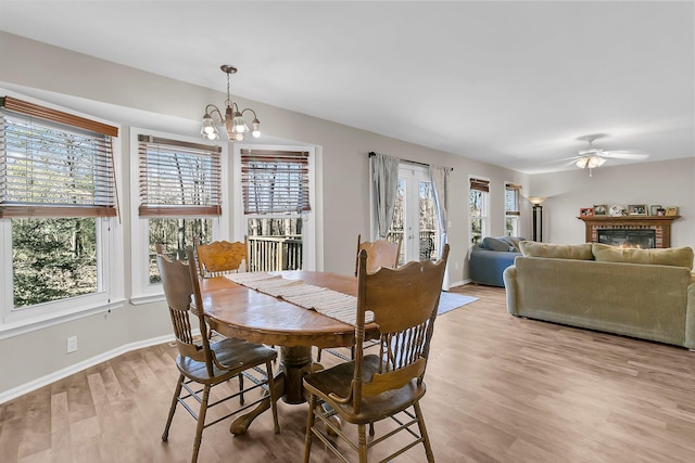 dining space with ceiling fan with notable chandelier, a wealth of natural light, a fireplace, and light hardwood / wood-style flooring