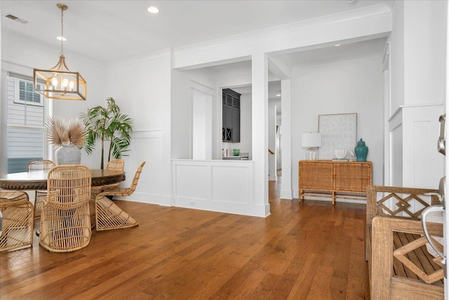 dining space featuring a chandelier, a decorative wall, wood finished floors, ornamental molding, and recessed lighting