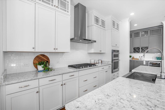 kitchen with white cabinets, stainless steel appliances, light stone counters, and wall chimney exhaust hood