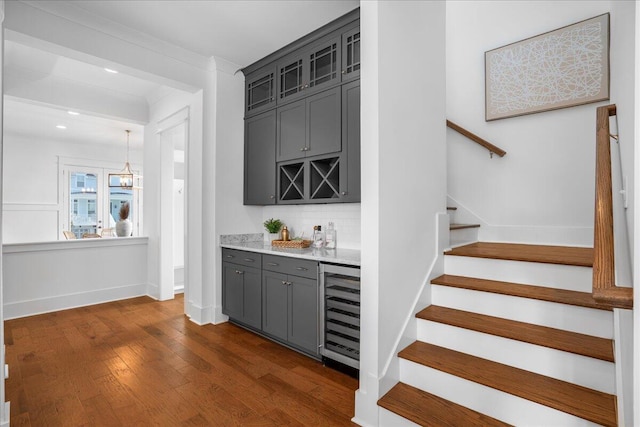 indoor wet bar with wine cooler, dark wood finished floors, backsplash, stairs, and baseboards